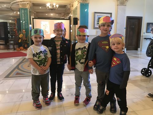 A group of five young boys pose for a photo while wearing the paper hat crafts they just made.