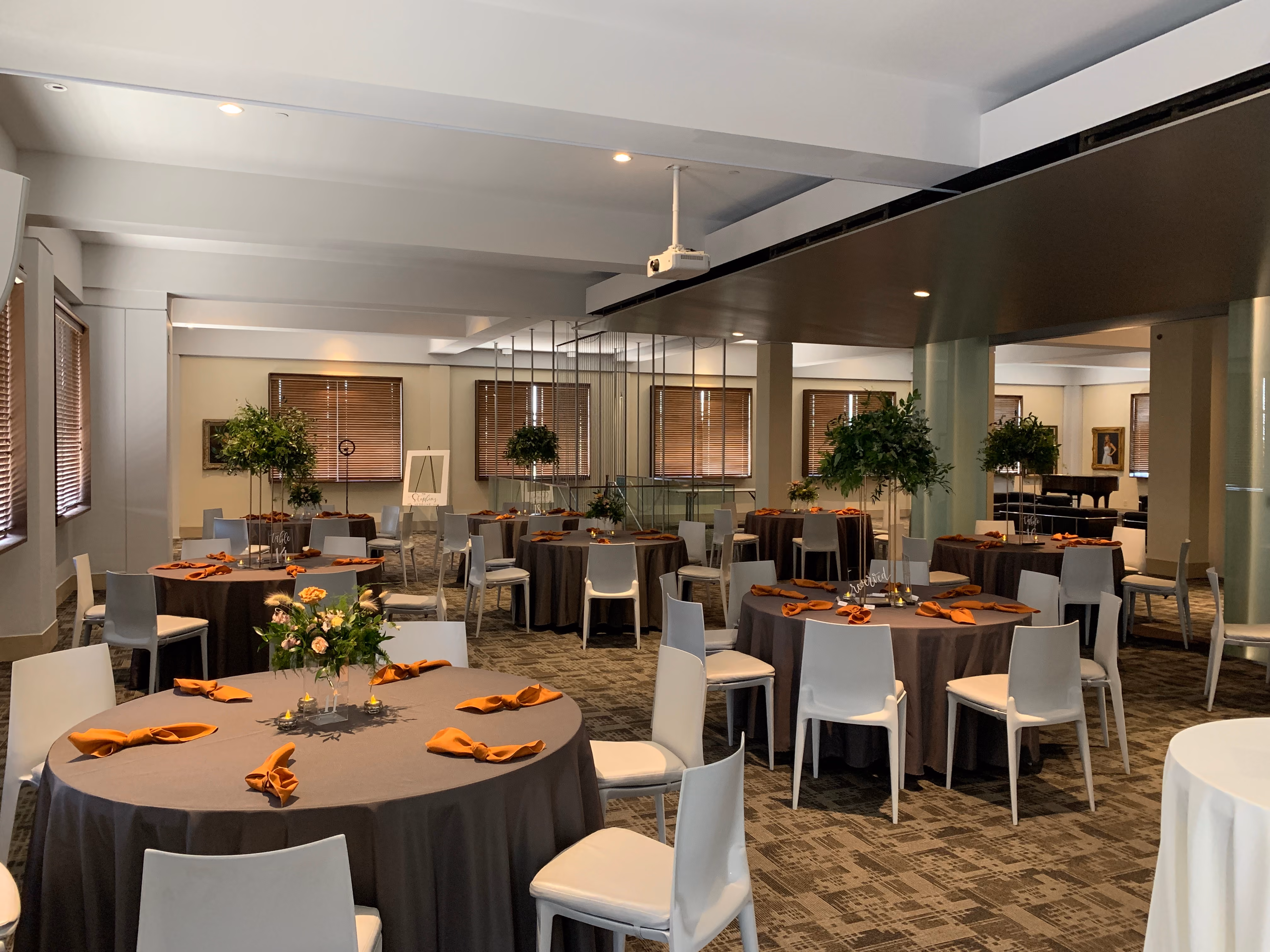 The Great Hall is prepared for an upcoming event, filled with tables set with silverware, orange napkins, and floral arrangements. 