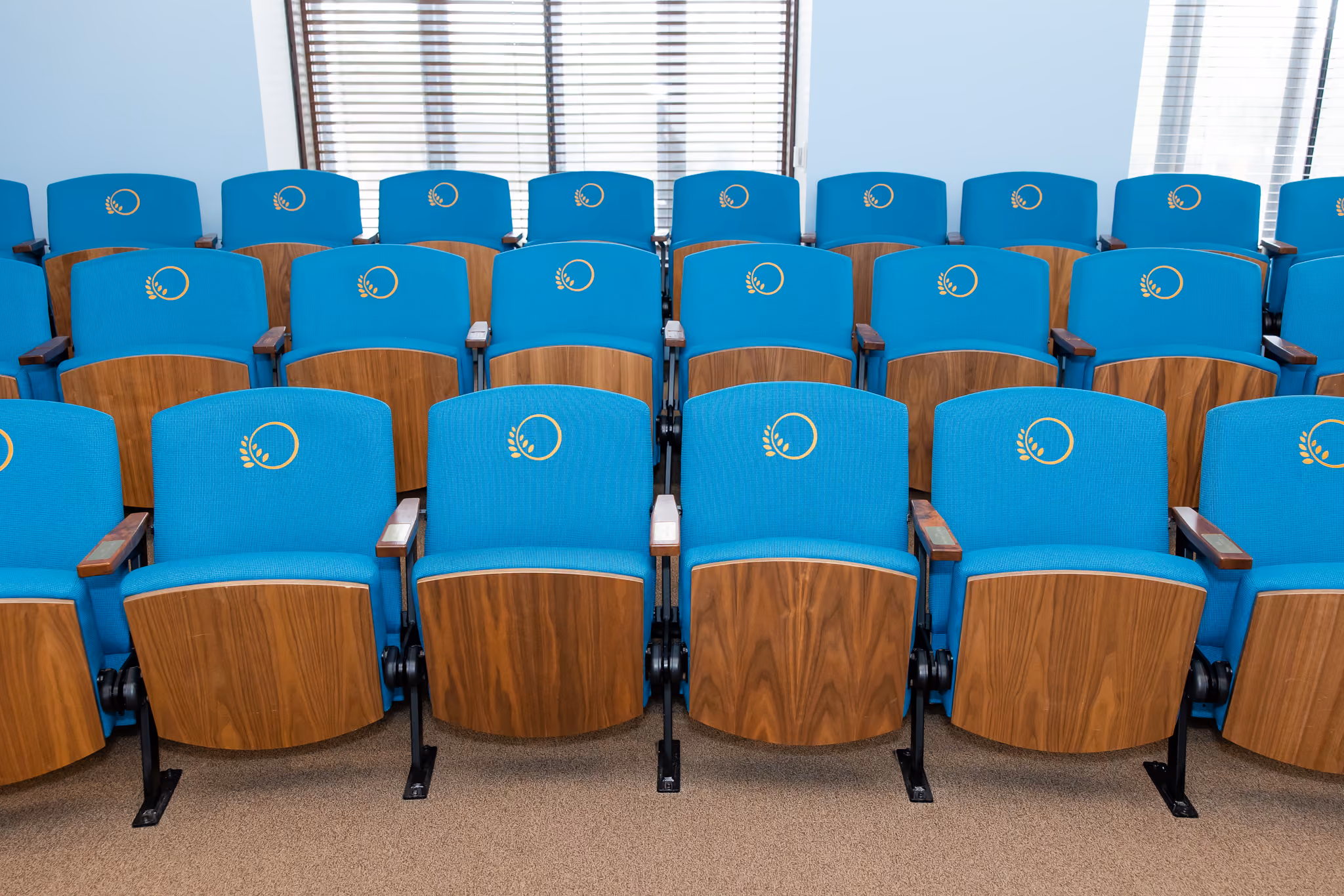 The Chesapeake Oklahoma Theatre contains three tiered rows of teal fabric movie theater-style chairs, each accented with the iconic Oklahoma Hall of Fame logo stitched in gold on the back cushion. 