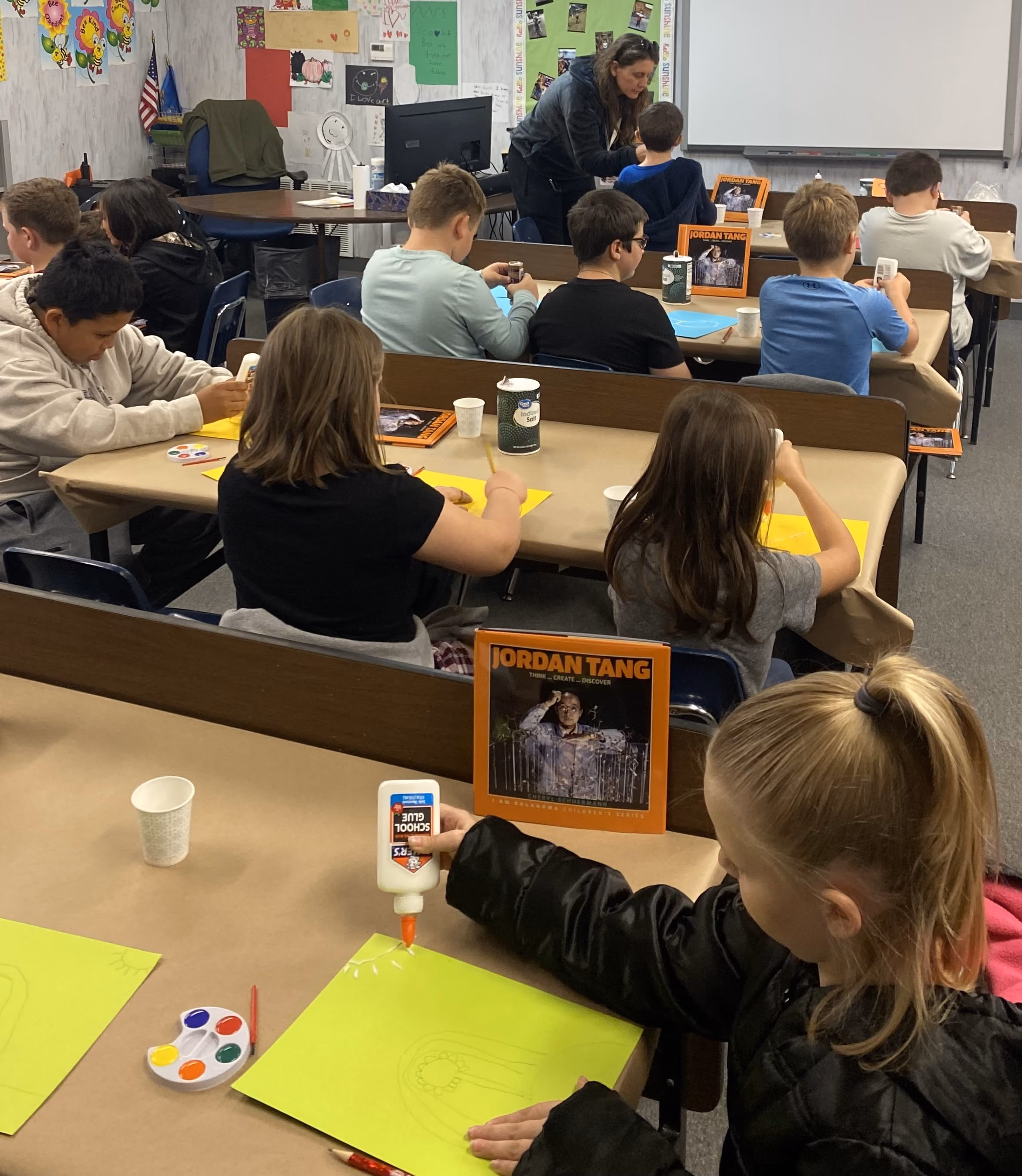 Elementary school students working on craft during an Oklahoma Originals program. Dr. Jordan Tang book is also displayed at a female student's desk.