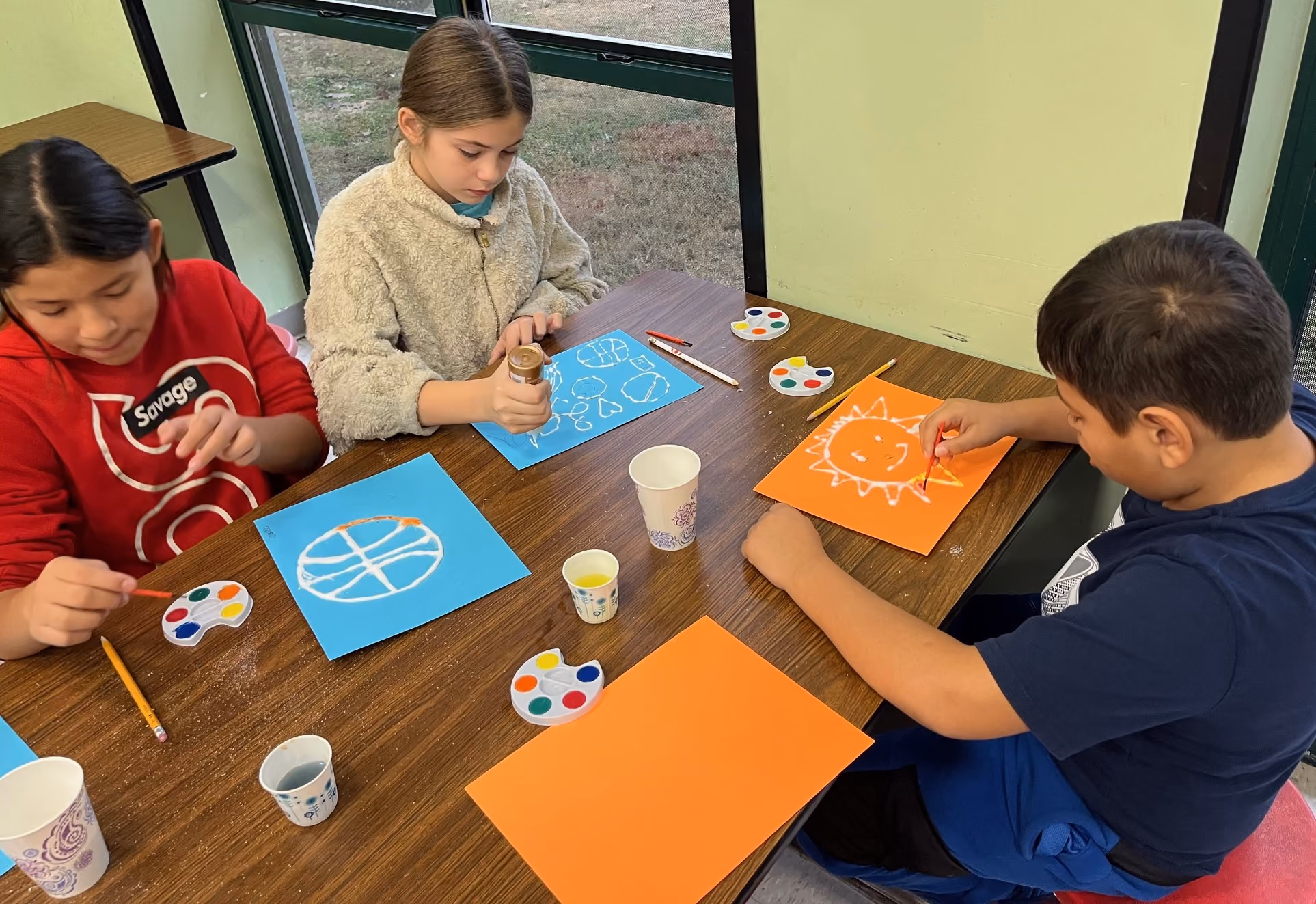 Three elementary school students creating salt rainbows with paper, glue, salt and watercolors during an Oklahoma Originals program.