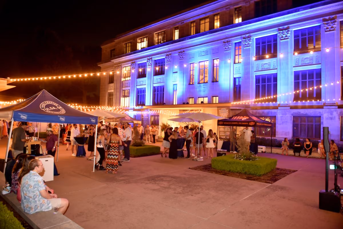 Dozens of guests wander around the Museum’s courtyard after sunset. Some groups visit brewery booths set up under pop-up tents, while others sit and converse on concrete planter benches.