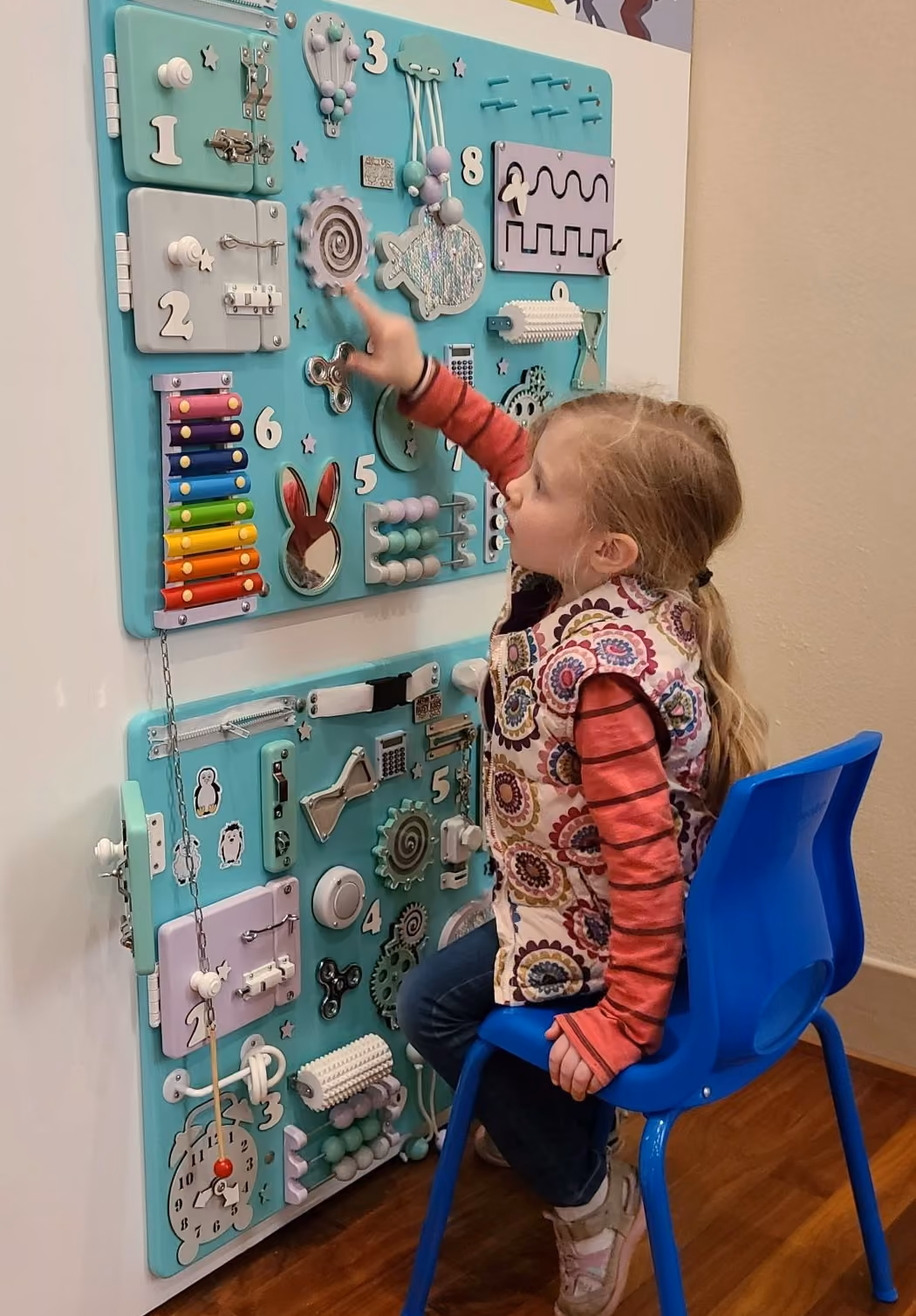 A young girl sits in a chair while playing with the various fidget toys on the museum’s sensory wall.