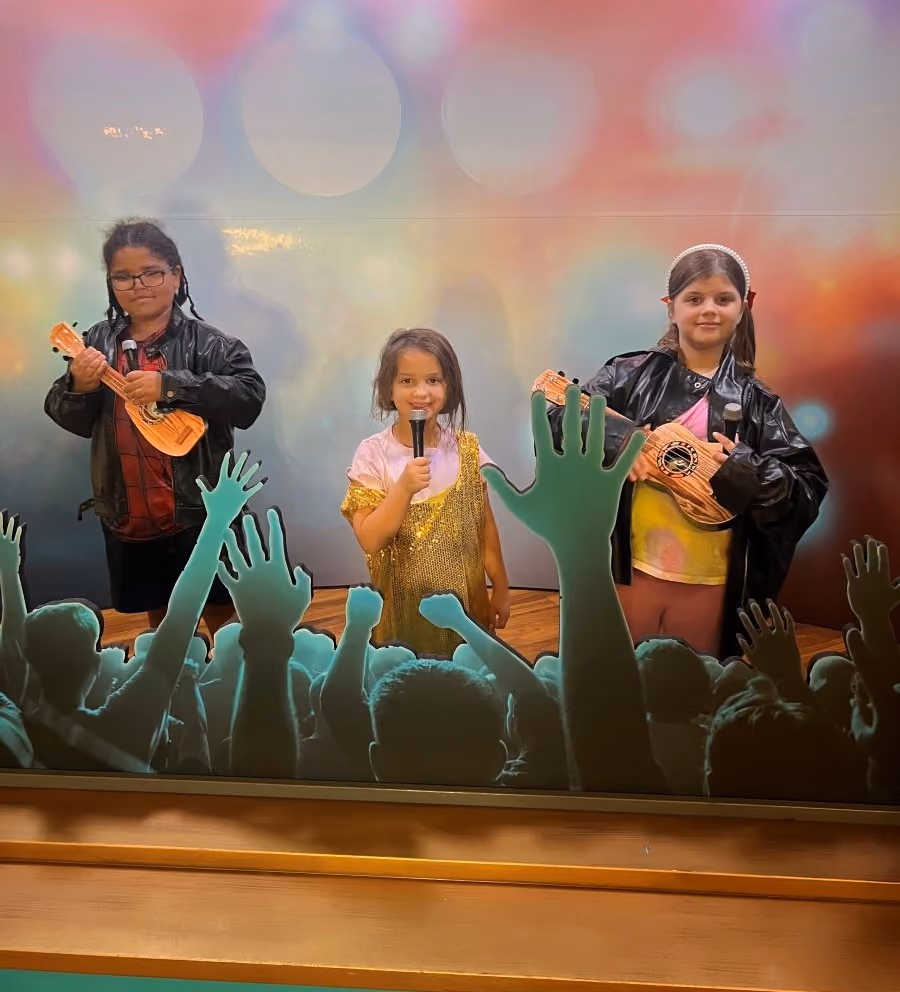Three elementary school aged girls dress up as musicians and singers in the Picture Yourself exhibit.