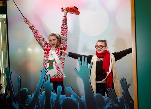 Two girls dressed in Christmas sweaters and scarves do a silly pose in the Picture Yourself exhibit.