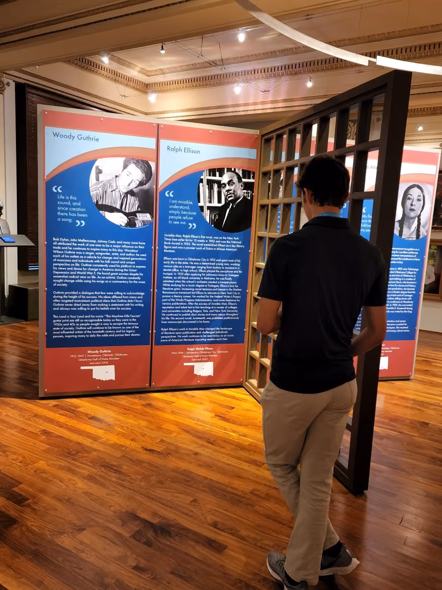 A high school aged boy looks at an exhibit panel in the museum highlighting Woody Guthrie and Ralph Ellison.