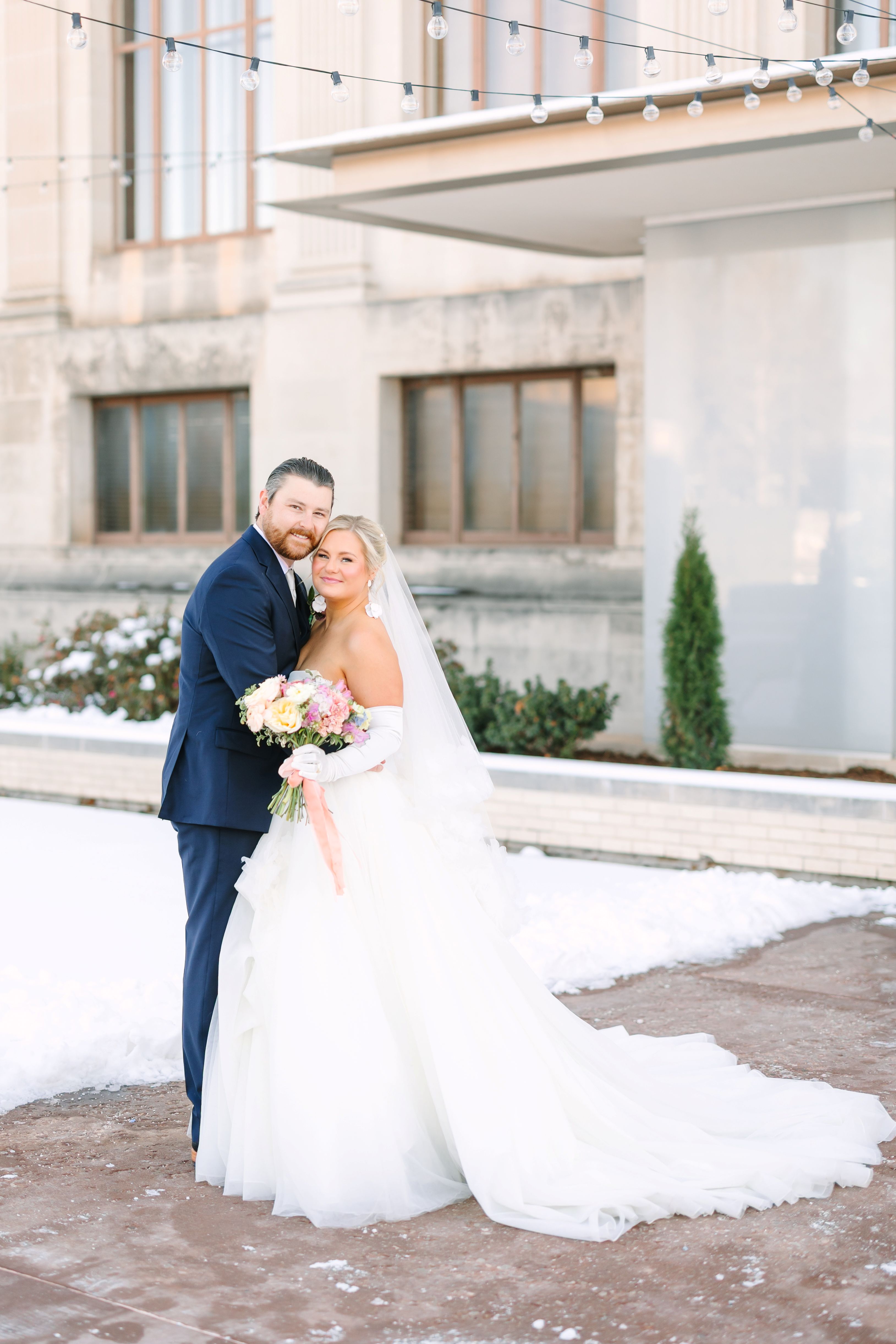 A bride and groom pose in the Oklahoma Hall of Fame garden in the snow.