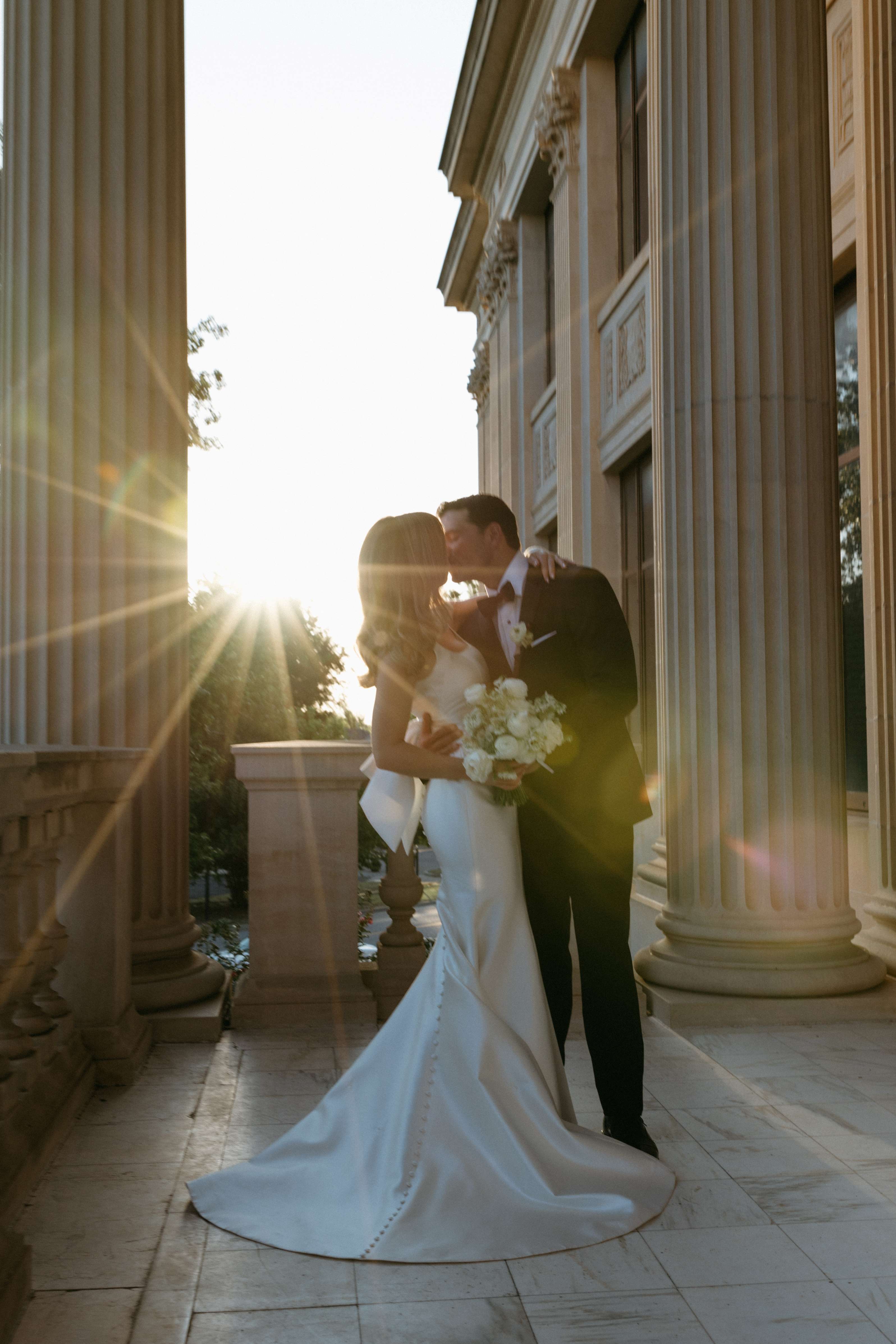 A bride and groom kiss in front of the front columns of the Oklahoma Hall of Fame.