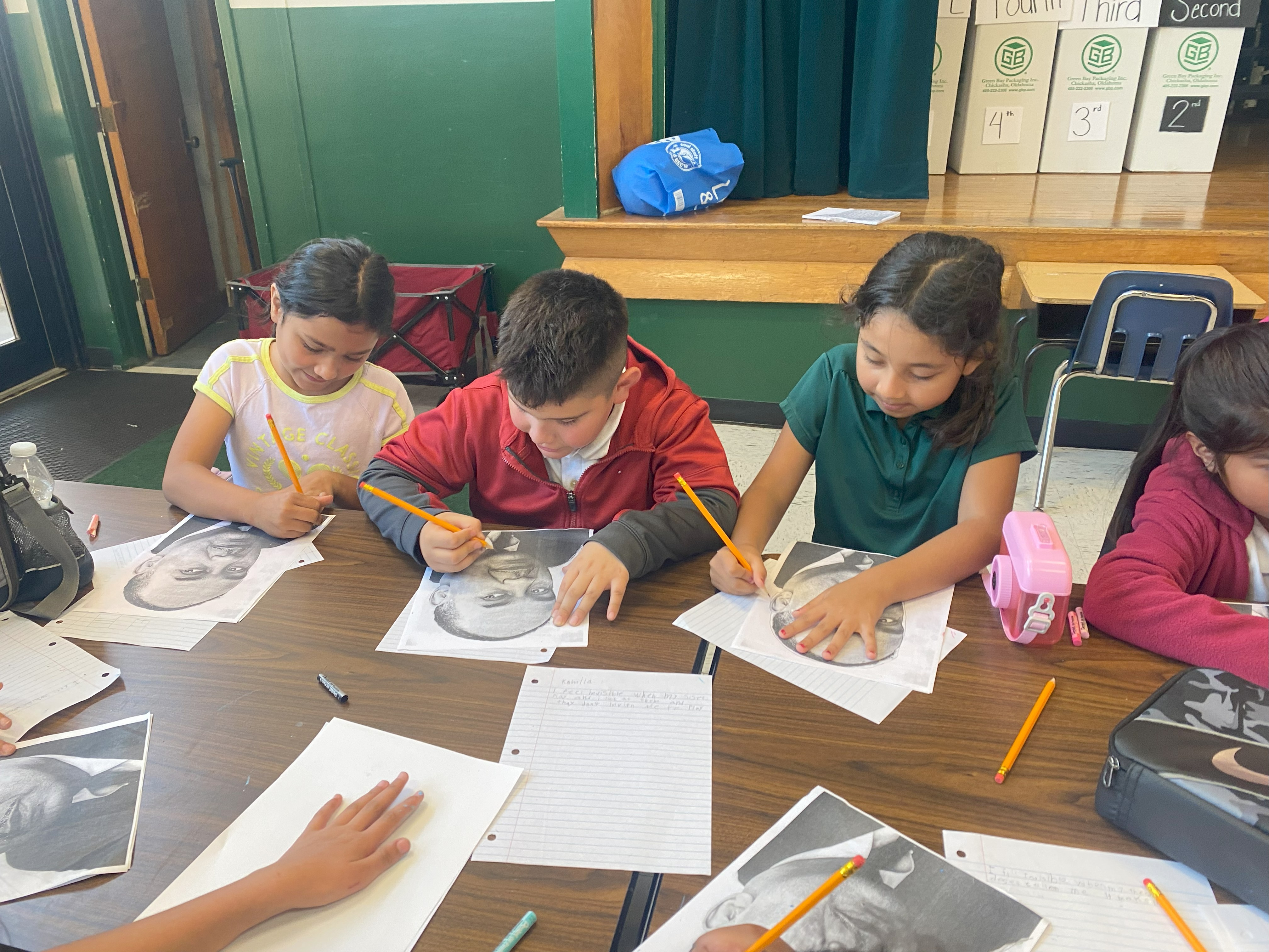 Three elementary school students trace photos of Ralph Ellison with pencils, as part of the Oklahoma Originals program.