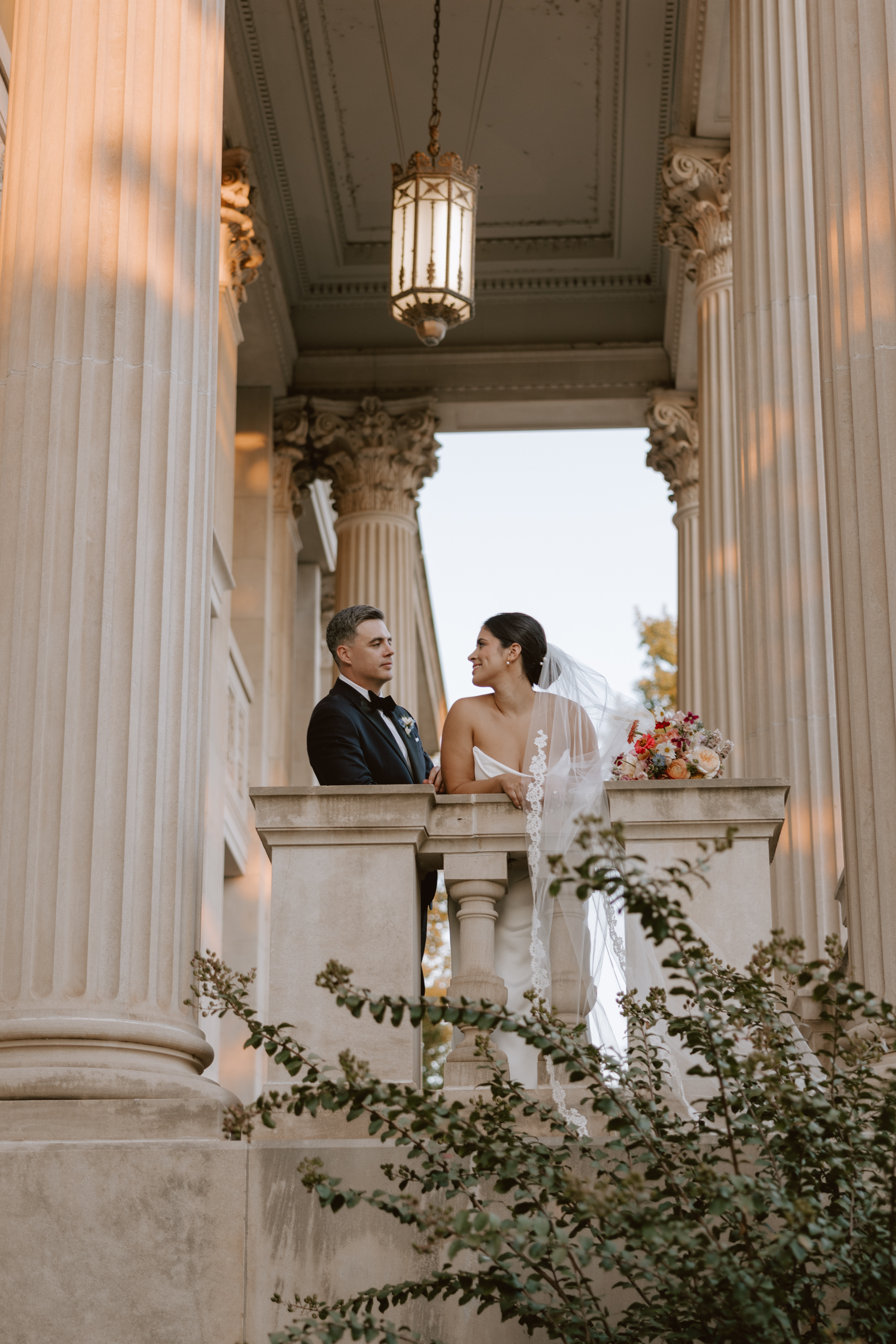 A bride and groom with the front columns of the Oklahoma Hall of ame