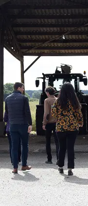 Groupe de visiteurs devant un hangar agricole avec tracteur