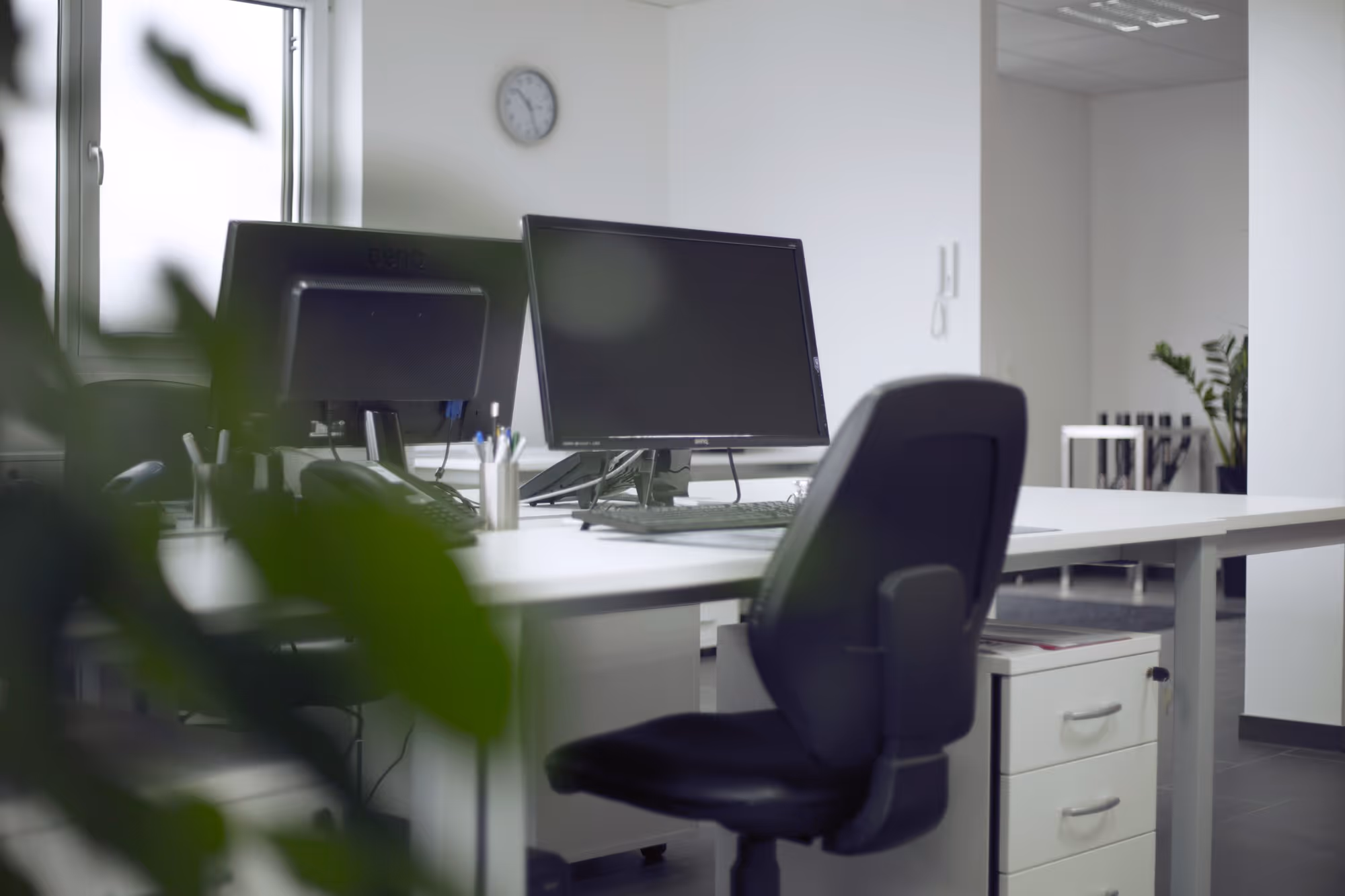 Pracovní místo v kanceláři s bílým kancelářským nábytkem, na kterém je černá obrazovka