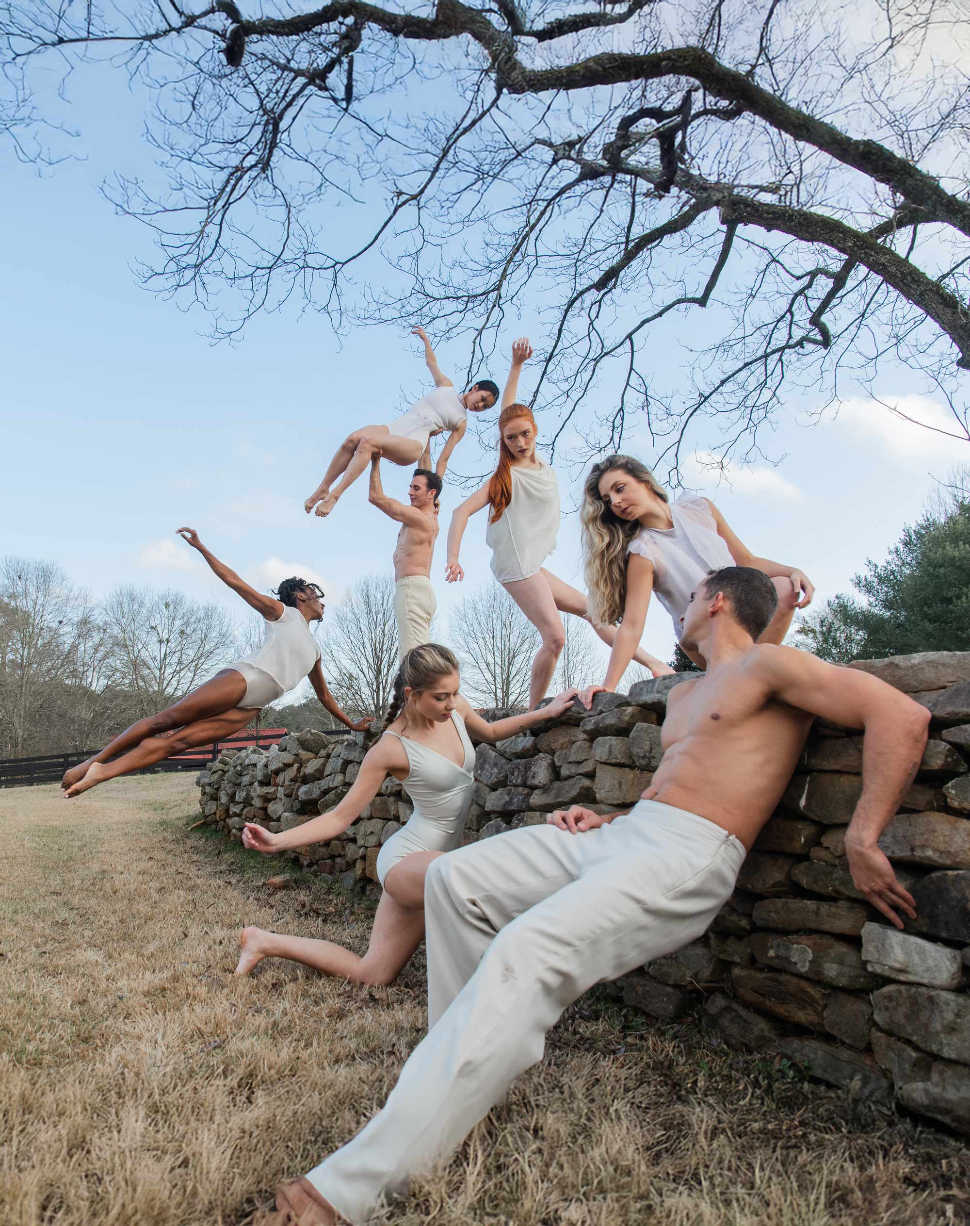 Contemporary dancers performing on a stone wall in nature, captured mid-movement