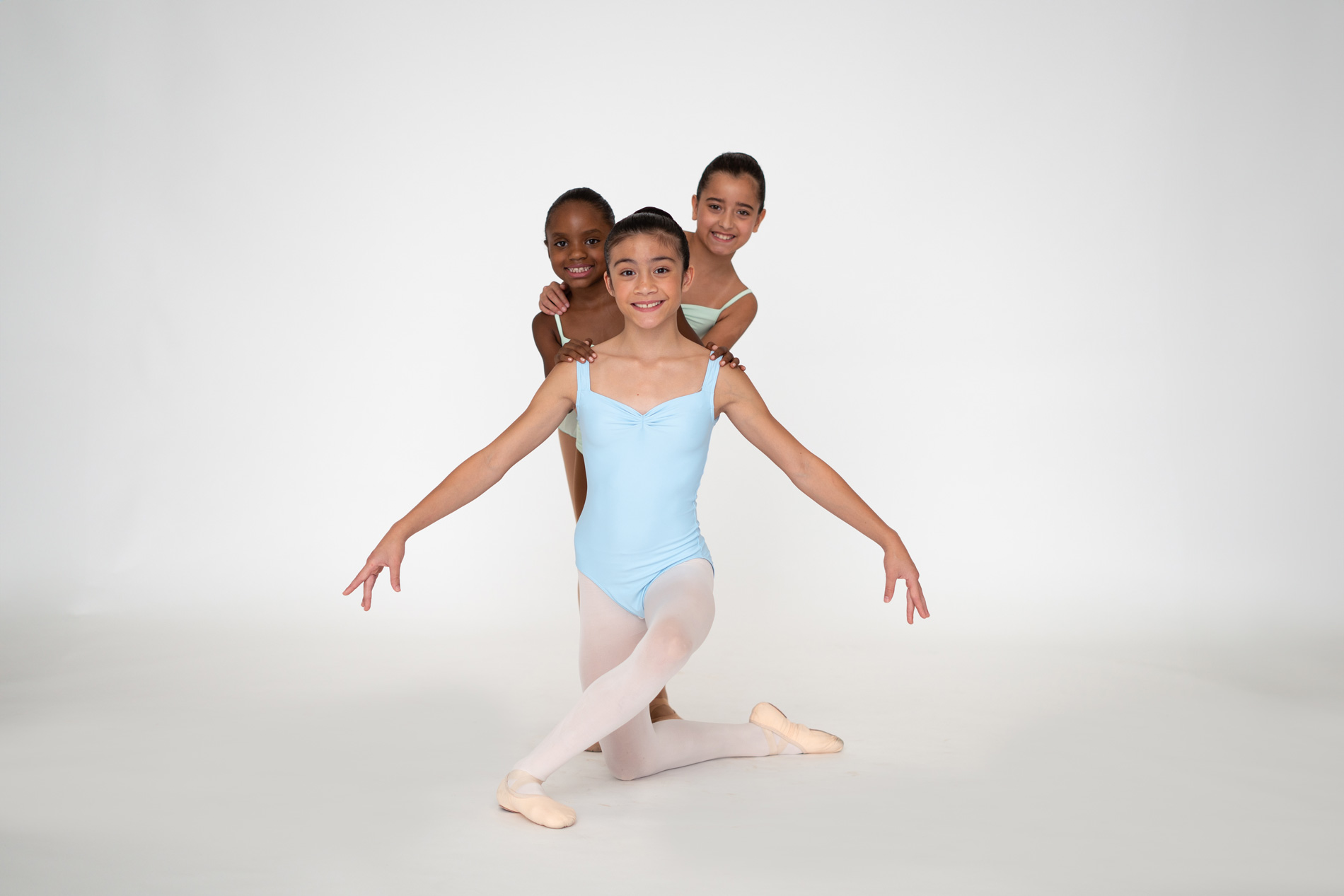 Three young ballet students posing in pastel leotards in a dance studio