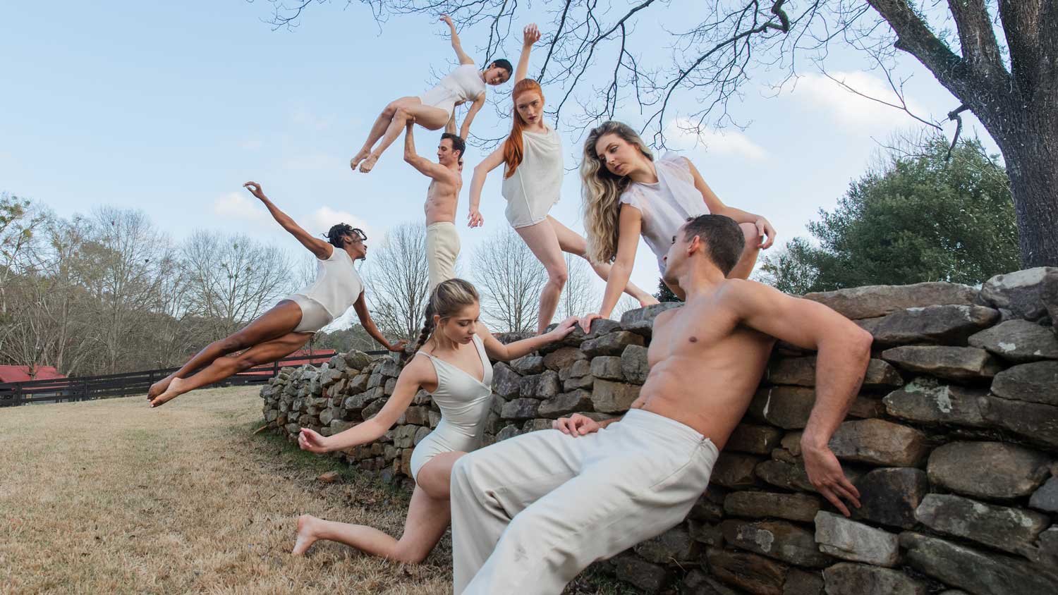 Contemporary dancers performing on a stone wall in nature, captured mid-movement