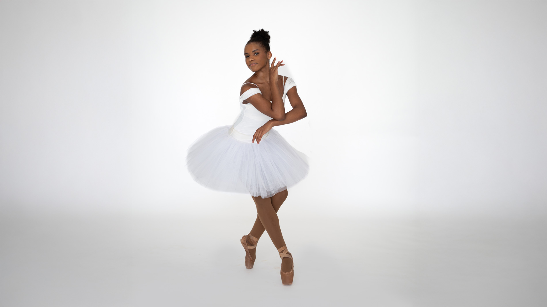 Black ballerina in white tutu posing en pointe in a ballet studio