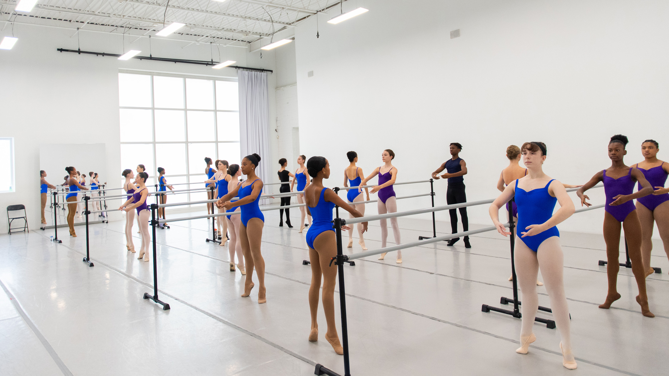 Ballet students practicing at the barre in a bright dance studio.