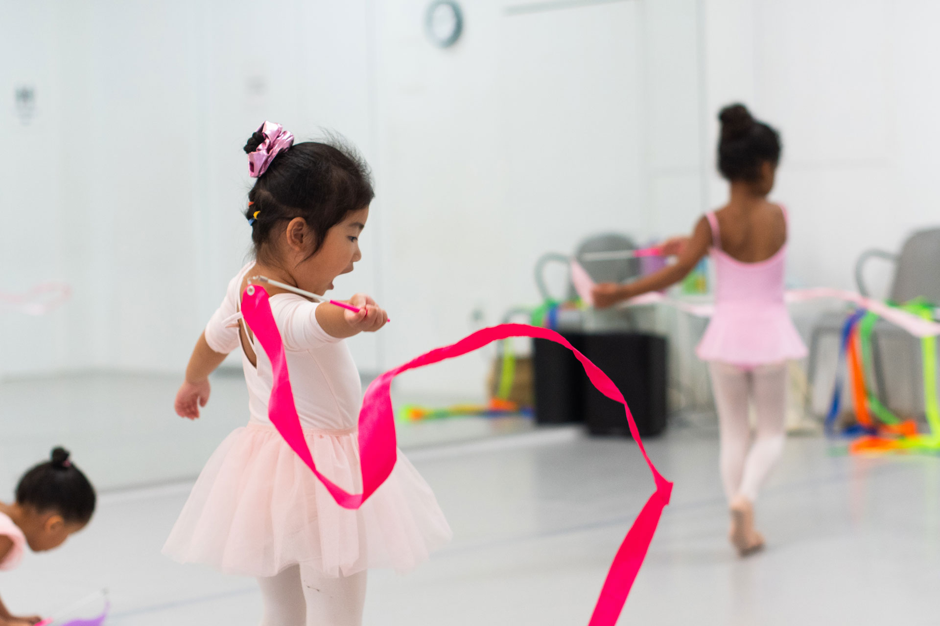Young children in pink tutus dancing with colorful ribbons.