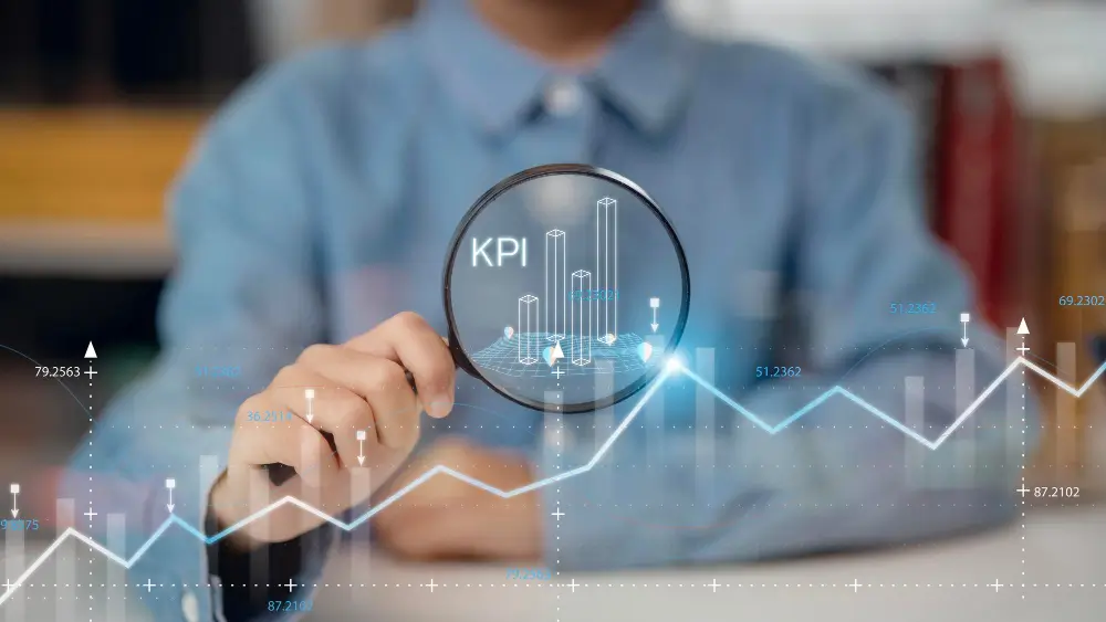 A person holds a magnifying glass focusing on the acronym 'KPI' and several 3D digital bar charts.