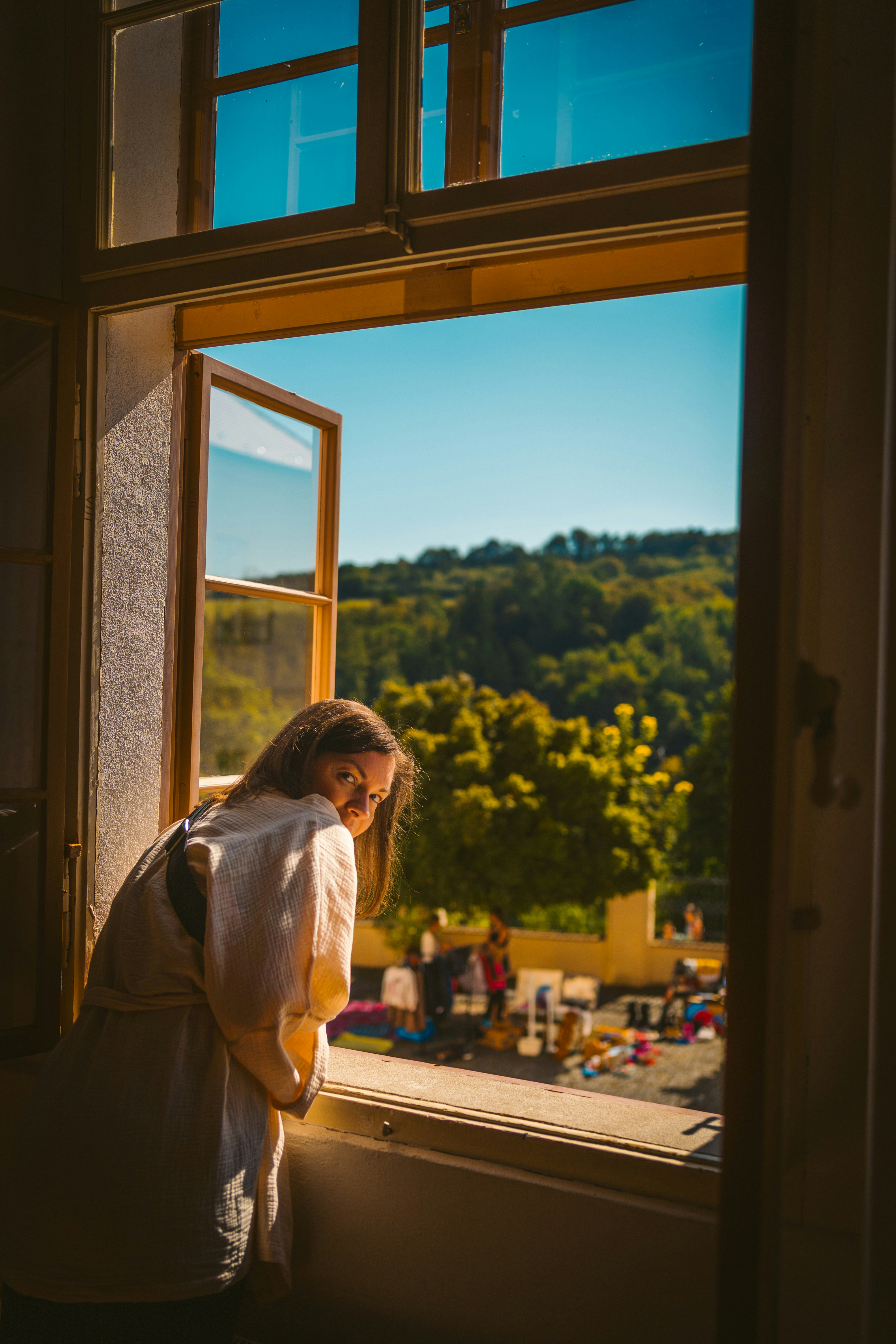 Person leaning out of an open window overlooking a scenic hillside, representing perspective and future planning.
