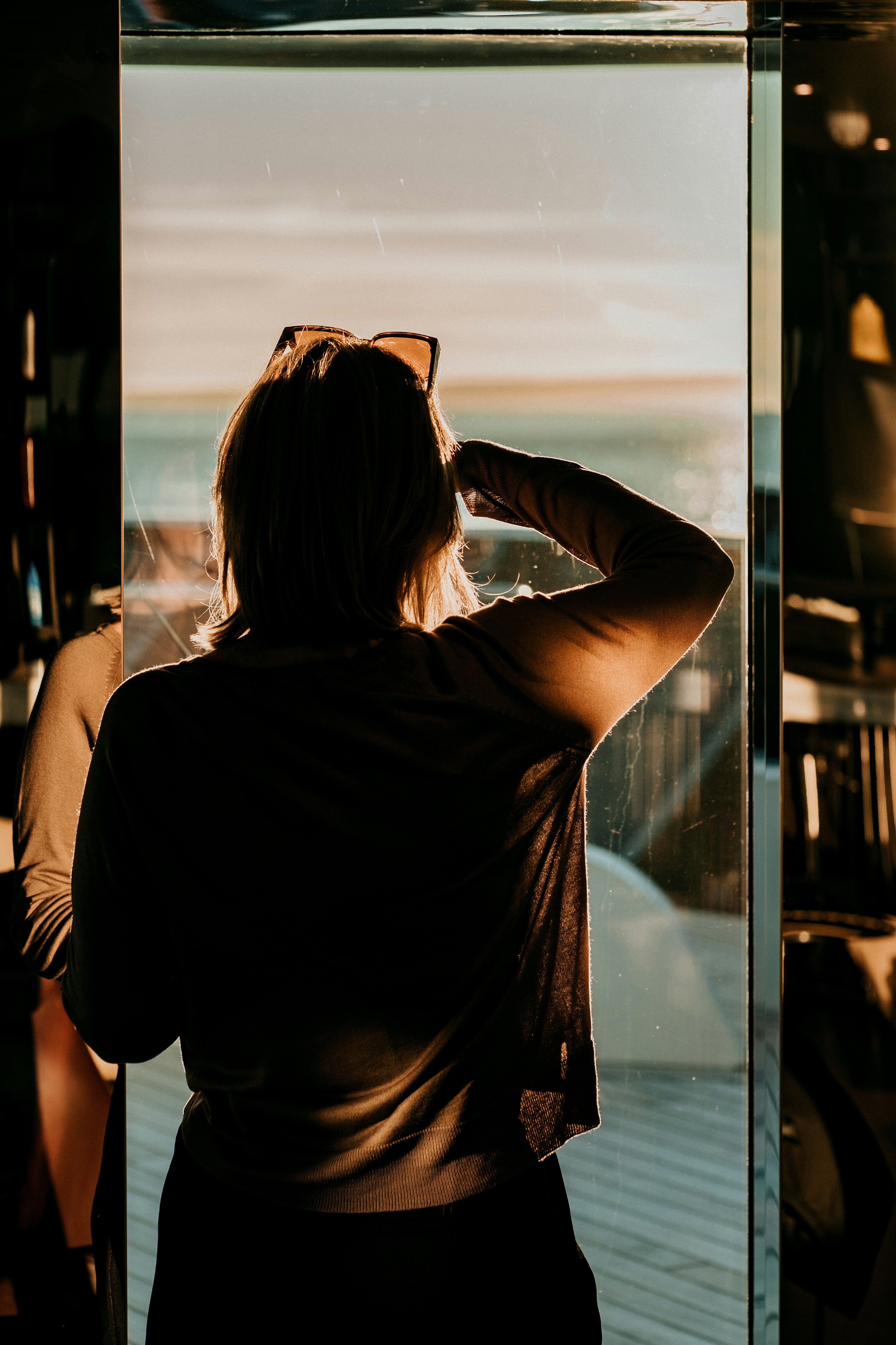 Person standing by a window at sunset, looking outside, representing reflection and future planning.