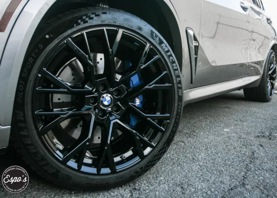 Gloss black powder coated wheel on a BMW with blue brake calipers, finished at Espo's Powder Coating in NJ
