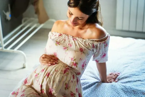 kobieta w ciąży leży na łóżku trzymając się za brzuch | od kiedy trzeci trymestr