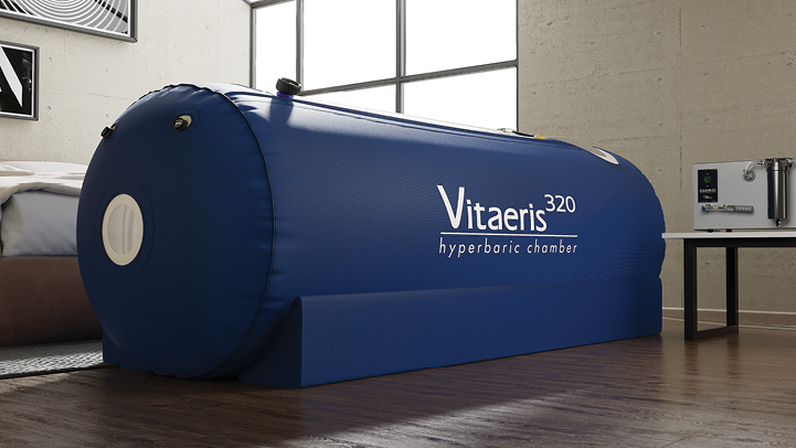 Blue Vitaeris 320 hyperbaric chamber set on wooden floor in a modern room with large window.