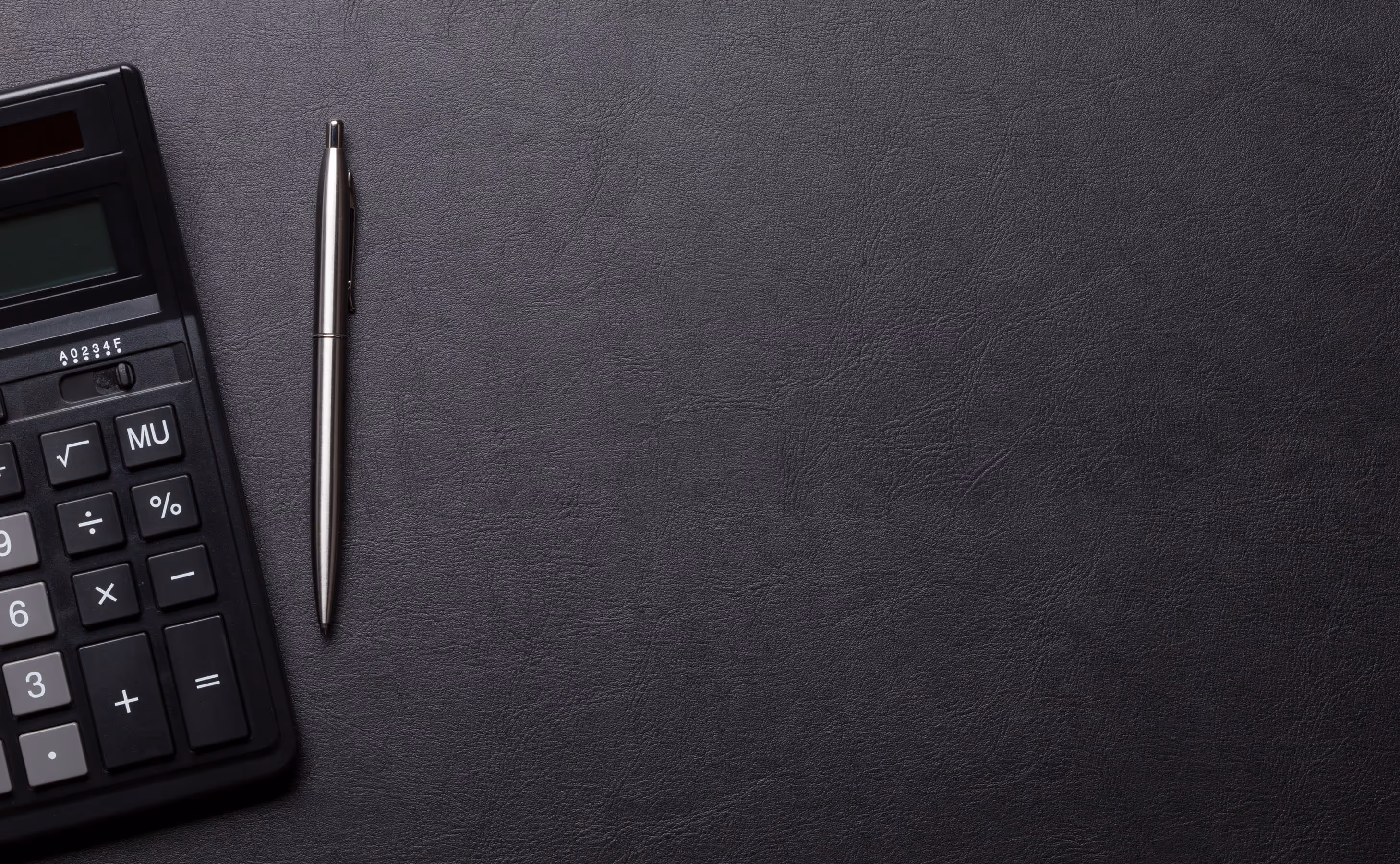 Black calculator and silver pen on a textured dark leather surface.