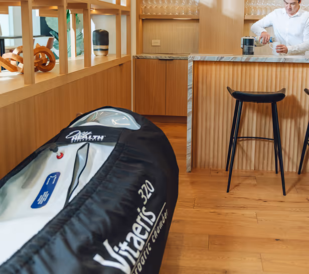 Modern kitchen with wooden floor and bar stools, and a Black Vitaris 320 Hyperbaric Chamber in the foreground.