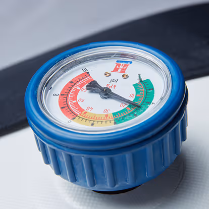 Close-up of a blue tire pressure gauge showing pressure readings in psi with colored zones for safe and unsafe levels.