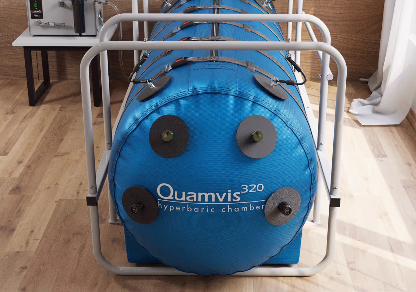 Blue Quamvis 320 hyperbaric chamber secured in a metal frame with valves on the front, placed on a wooden floor indoors.