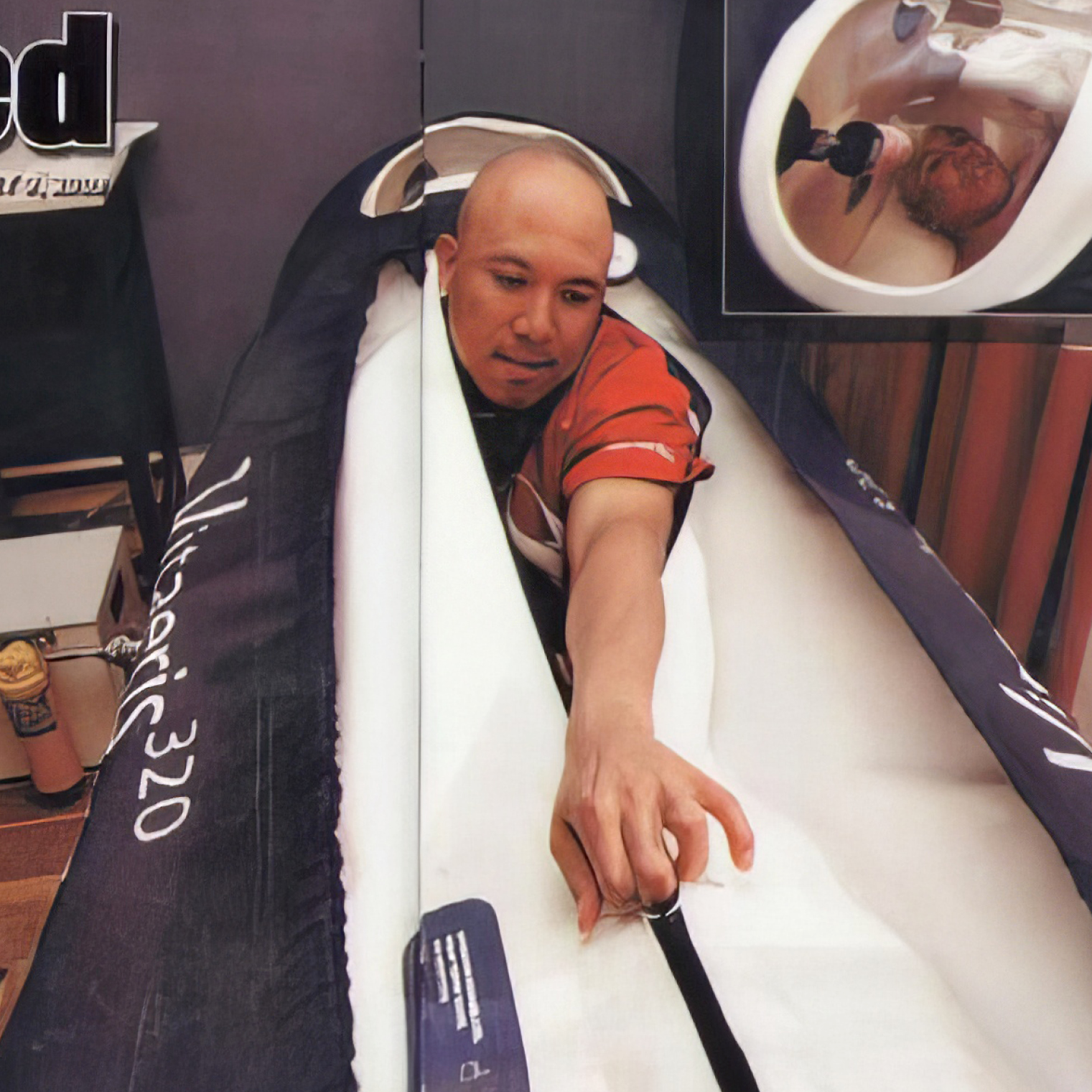 Man lying inside a narrow, Vitaeris 320 hyperbaric chamber, reaching forward with one hand.