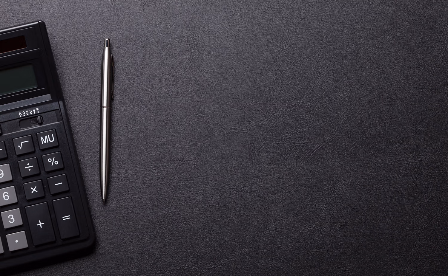 Black calculator and silver pen on a textured dark leather surface.