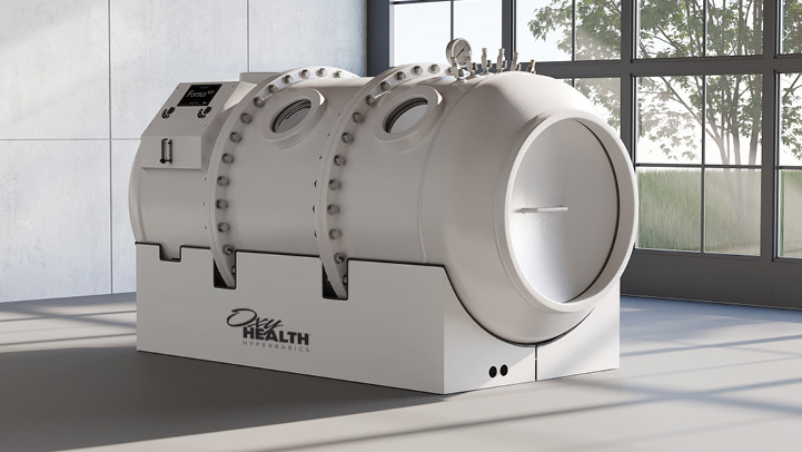 A modern hyperbaric oxygen therapy chamber with two round viewing windows and control panel in a bright room with large windows and concrete walls.