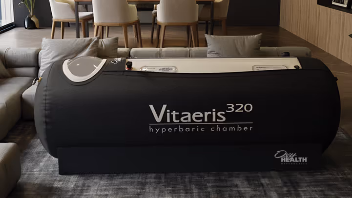 Black Vitaeris 320 hyperbaric chamber placed in a modern living room with a sofa and chairs around it.