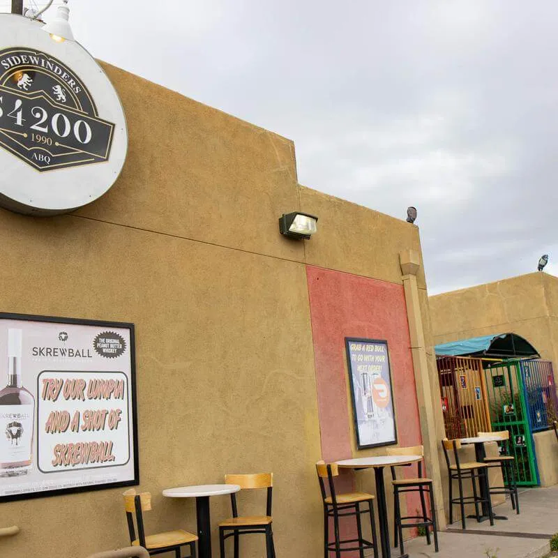 Exterior of the bar and grill with a fence displaying the LGBTQ+ flag and different banners on the wall that promote an inclusive and welcoming atmosphere