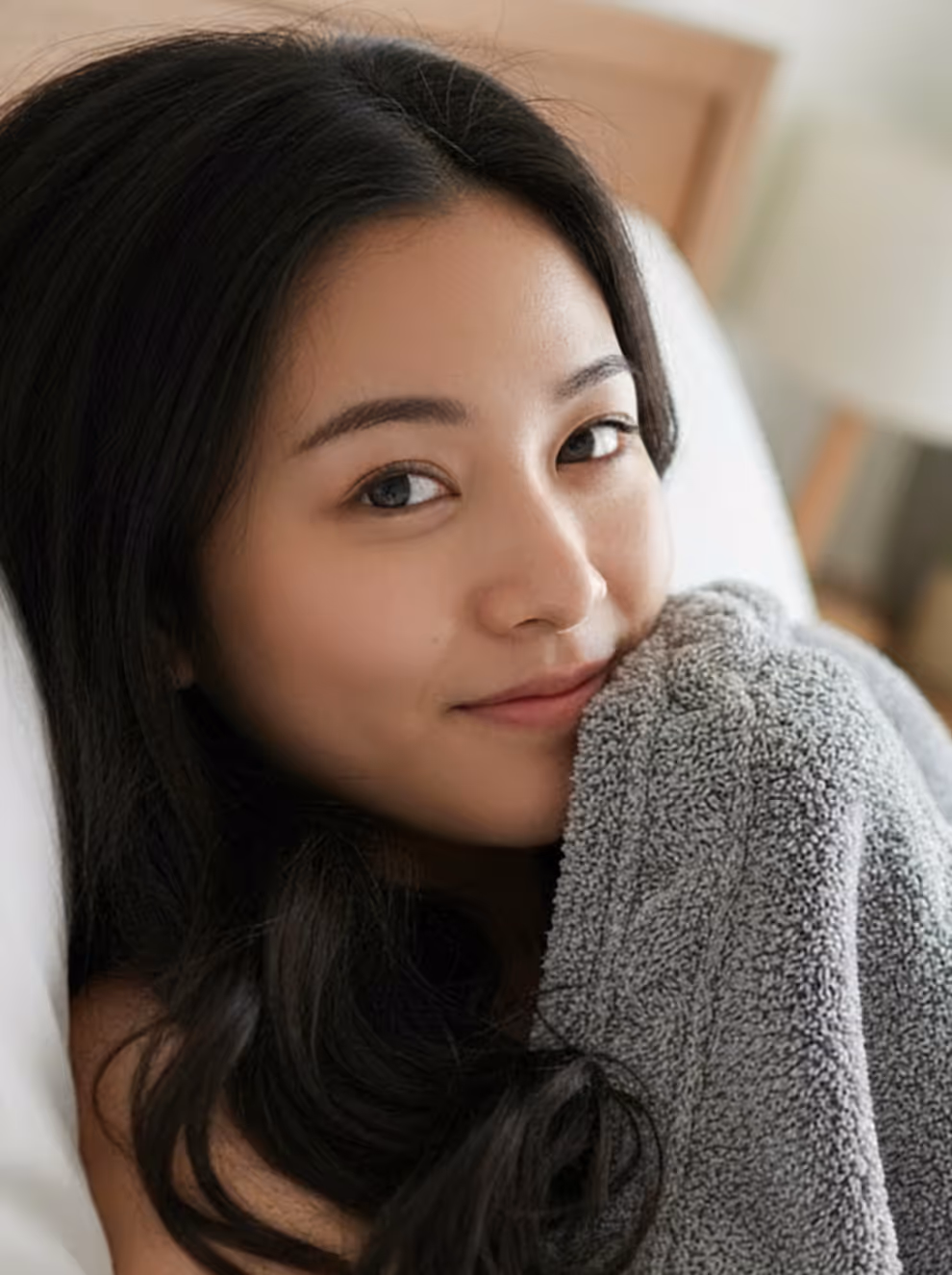 A Singapoean girl covered up to half of her face under the bedsheets