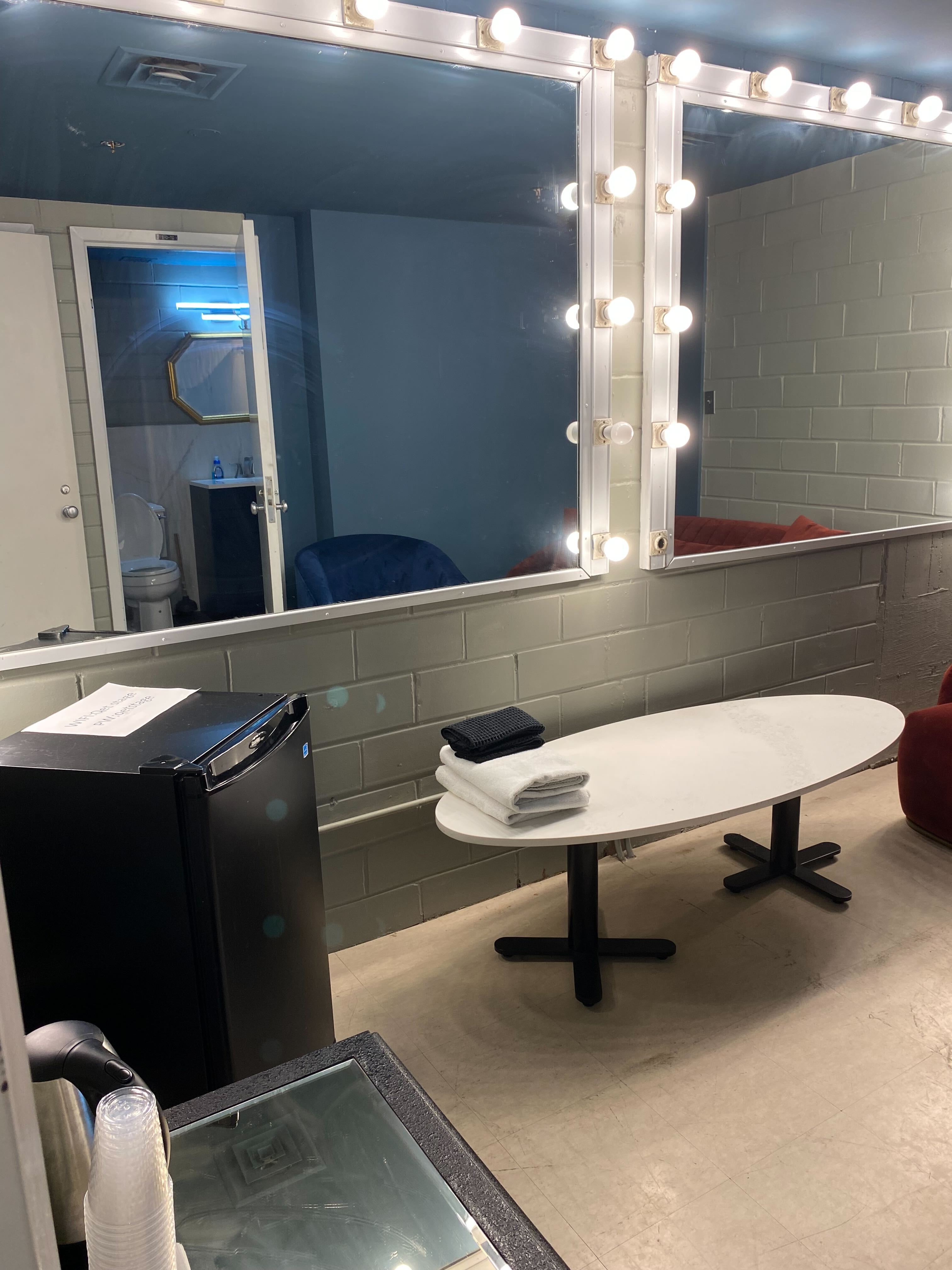 Dressing room fridge, lit mirrors, table, and adjoining bathroom