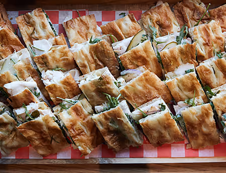 Tray of focaccia sandwiches cut into small squares with greens and cheese