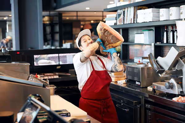 Photo of Erika behind the counter of Due Madri holding a large hunk of meat