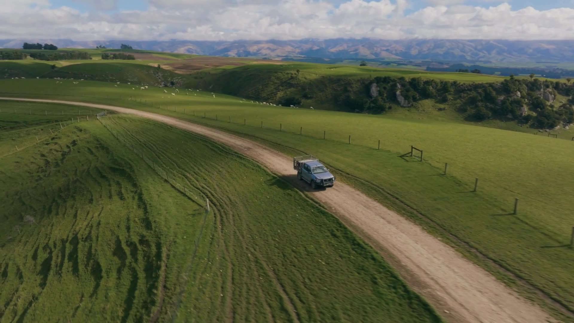 Aerial view of a farm ute driving along a track across green hills
