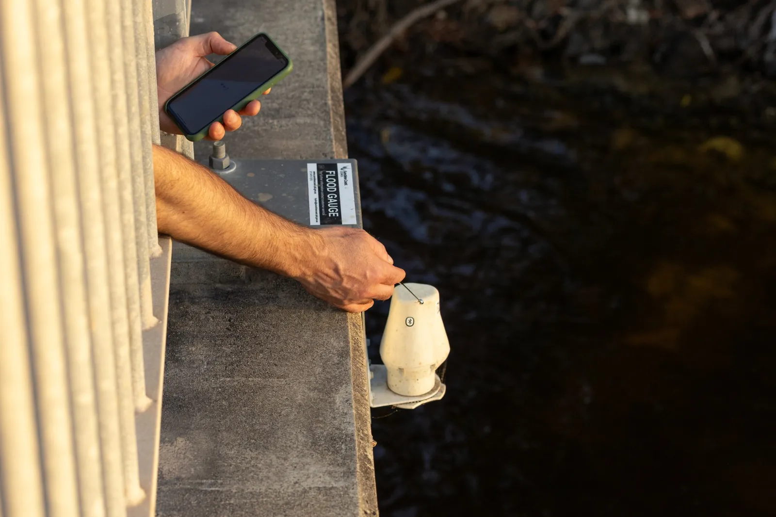 Field technician commissioning a HiLo LS1-R flood gauge on a bridge from a phone