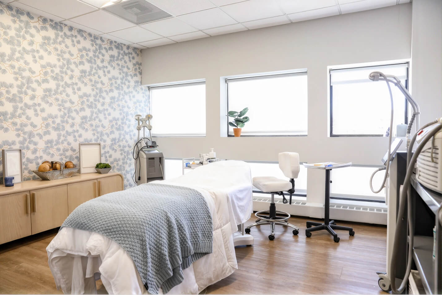 Reception area with a white desk, wall-mounted circular shelves holding skincare products, and a large framed line art of a woman with towel on her head.