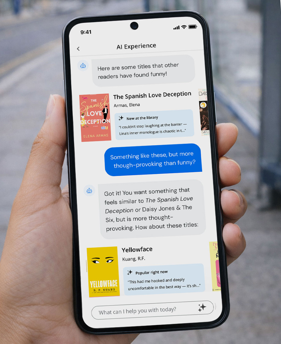 A person standing at an outdoor bus stop holds a cell phone displaying the BiblioCommons AI library assistant that recommends books similar to The Spanish Love Deception and Yellowface, offering a conversational approach to reading suggestions.