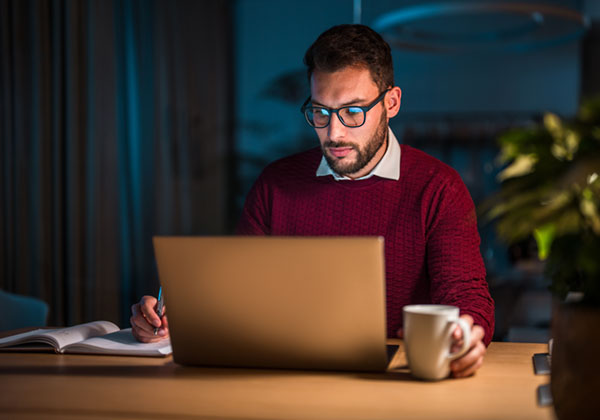 Man in a red sweater concentrating on his laptop in an office setting with a coffee cup by his side