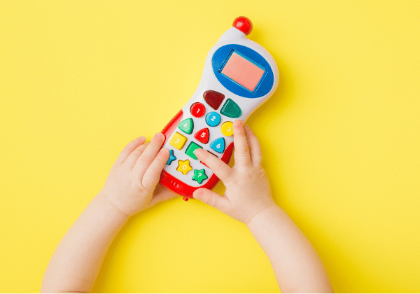 Baby hands playing with colorful toy of mobile phone on bright yellow table background