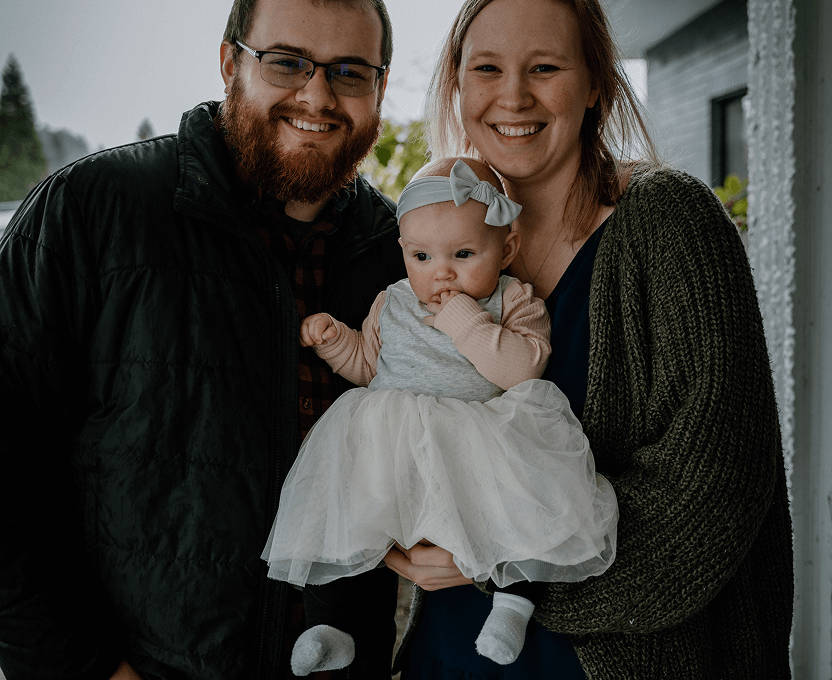 Smiling man and woman holding a baby dressed in a white tutu and light blue headband.