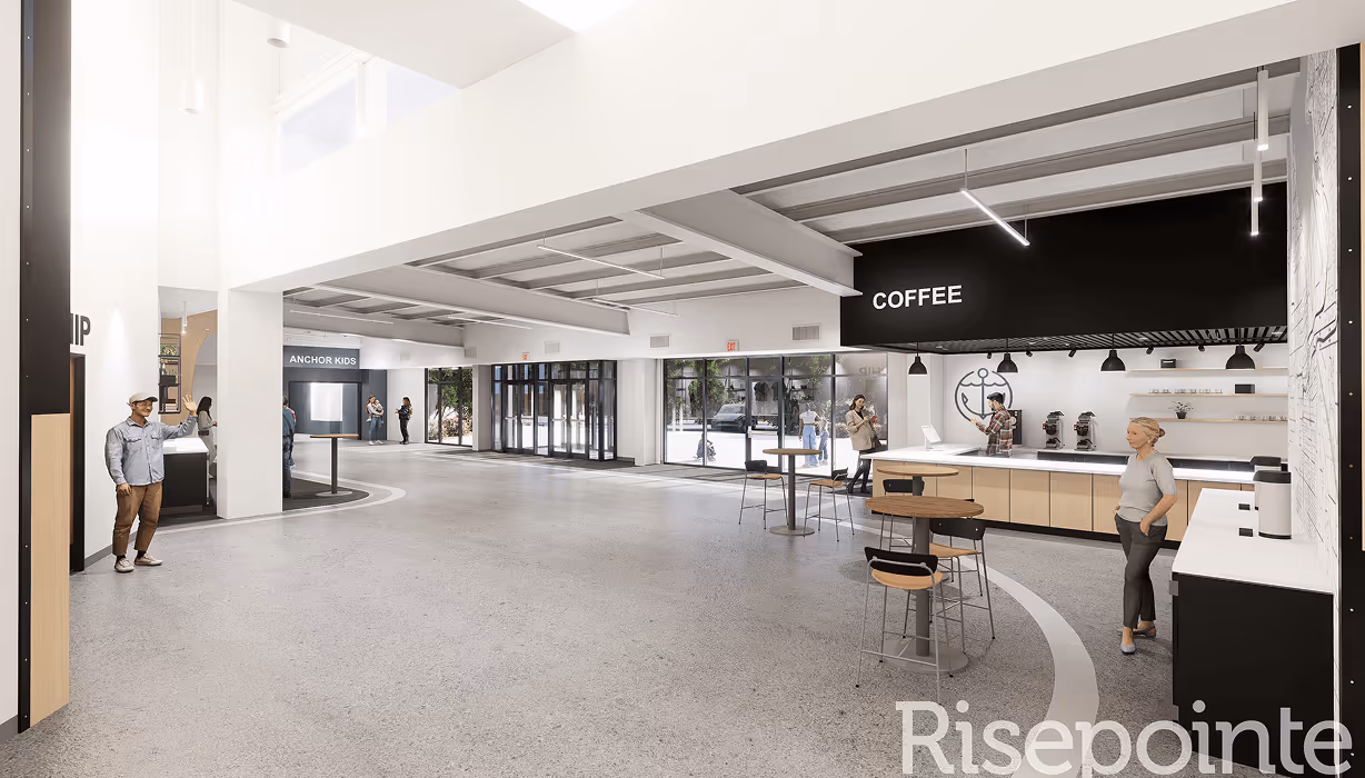 Modern open lobby with a coffee bar, round tables with chairs, and labeled areas for coffee and Anchor Kids.