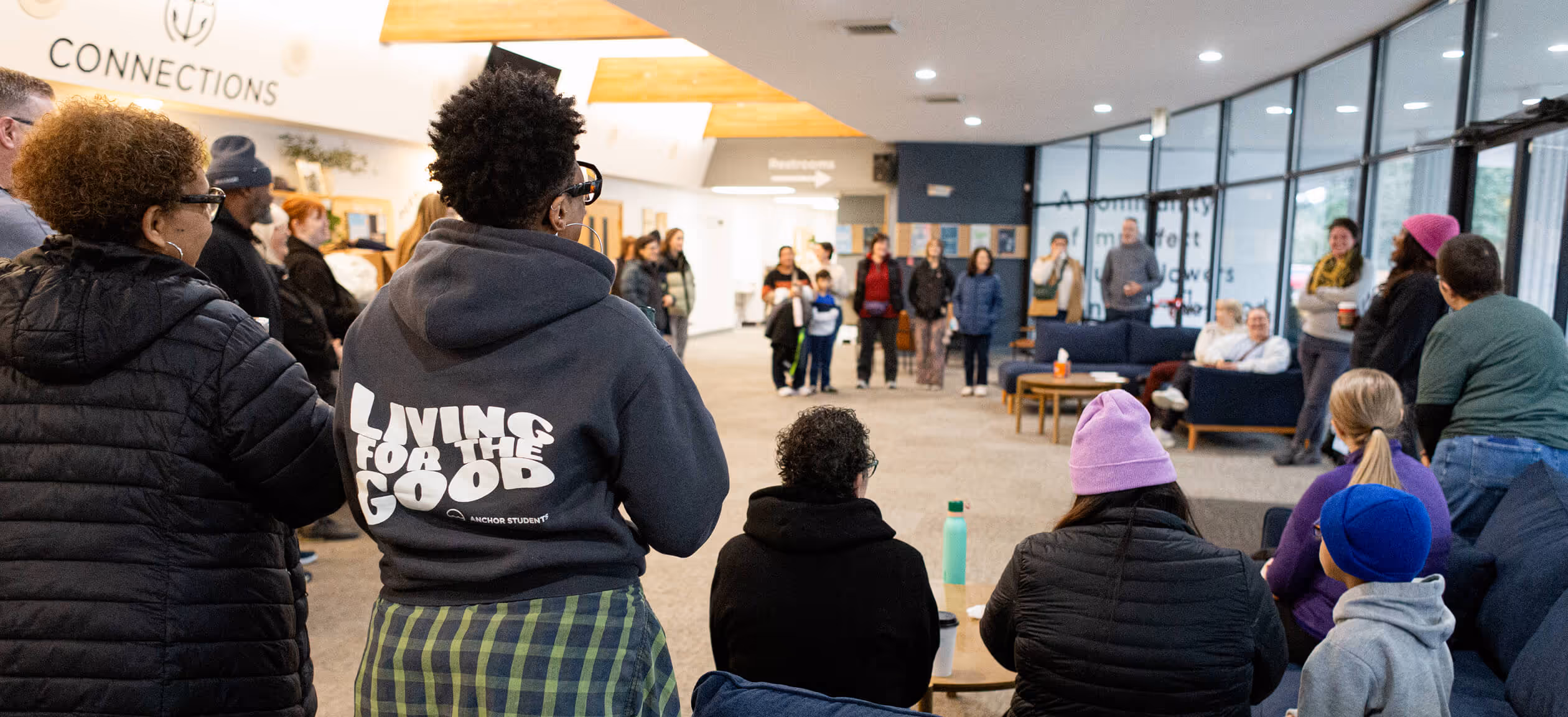 Group of people gathered indoors in a community space with some seated and others standing in a circle.